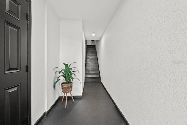 hall featuring baseboards, concrete floors, and stairs