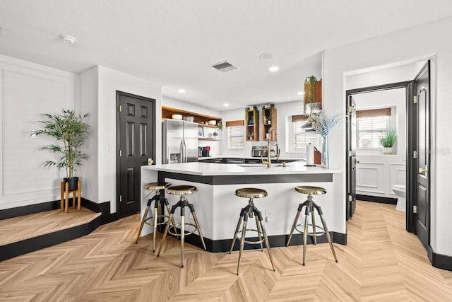 kitchen featuring open shelves, a breakfast bar, a peninsula, stainless steel refrigerator with ice dispenser, and visible vents