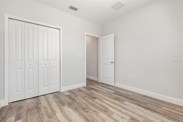 unfurnished bedroom featuring baseboards, a closet, light wood finished floors, and visible vents