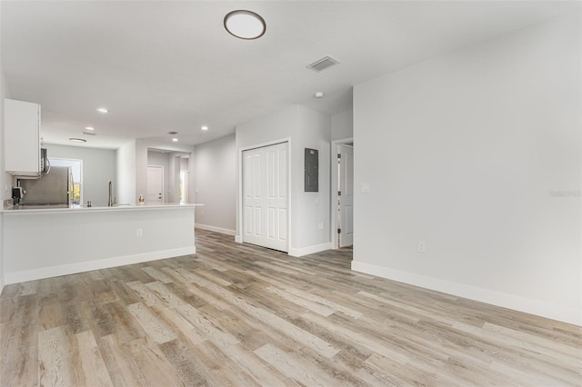 unfurnished living room featuring baseboards, electric panel, light wood-type flooring, and visible vents