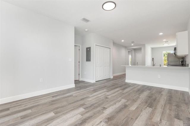 unfurnished living room featuring a sink, recessed lighting, baseboards, light wood-type flooring, and electric panel