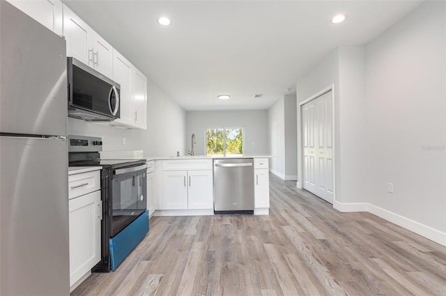 kitchen featuring a sink, a peninsula, stainless steel appliances, recessed lighting, and white cabinetry