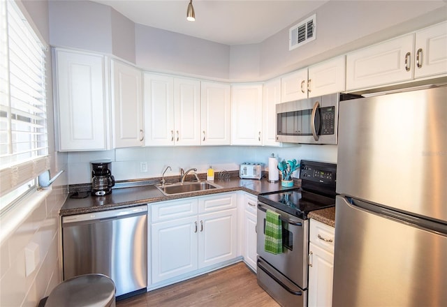kitchen with dark countertops, a sink, stainless steel appliances, white cabinetry, and visible vents