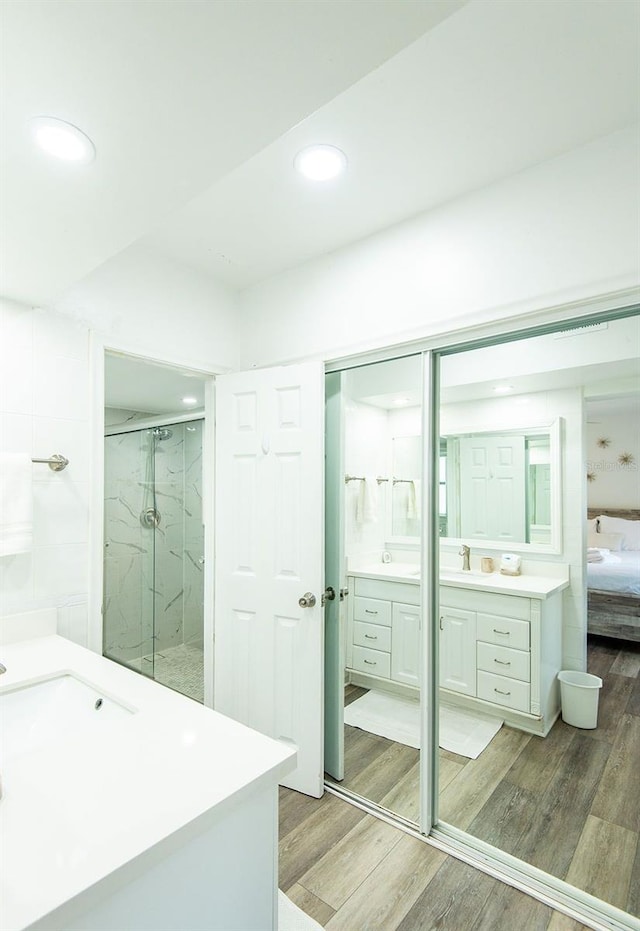 full bathroom featuring recessed lighting, a marble finish shower, wood finished floors, and two vanities