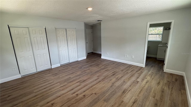 3188 Lake Saxon Dr, Land O Lakes, FL 34639 - unfurnished bedroom featuring two closets, a textured ceiling, baseboards, and wood finished floors