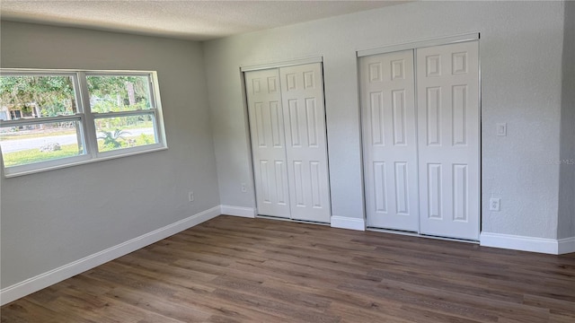 3188 Lake Saxon Dr, Land O Lakes, FL 34639 - unfurnished bedroom with baseboards, a textured ceiling, multiple closets, and dark wood-style flooring