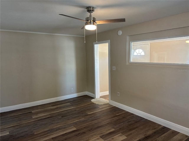 spare room featuring dark wood-style flooring, a ceiling fan, baseboards, and ornamental molding