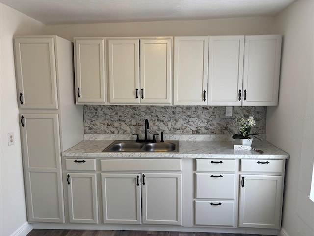 kitchen with white cabinets, baseboards, a sink, and tasteful backsplash