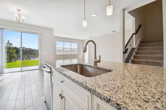 kitchen with light stone counters, a sink, dishwasher, a water view, and pendant lighting