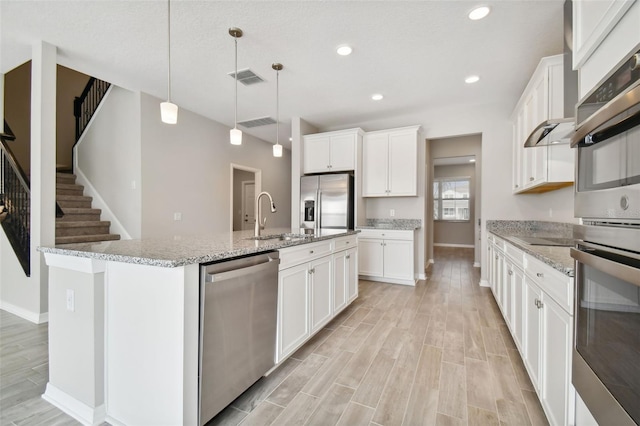 kitchen featuring a kitchen island with sink, visible vents, appliances with stainless steel finishes, a sink, and baseboards