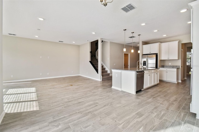 kitchen with visible vents, a kitchen island with sink, open floor plan, white cabinetry, and appliances with stainless steel finishes