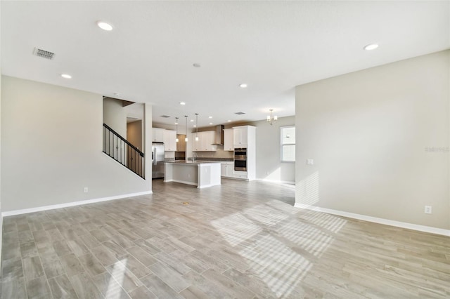 unfurnished living room with visible vents, recessed lighting, baseboards, and stairway