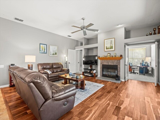 living area with a ceiling fan, visible vents, a fireplace, wood finished floors, and baseboards