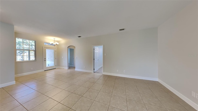 empty room featuring arched walkways, baseboards, a notable chandelier, and light tile patterned floors