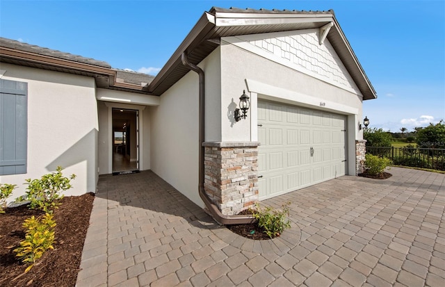 view of property exterior with a garage, fence, stucco siding, and stone siding