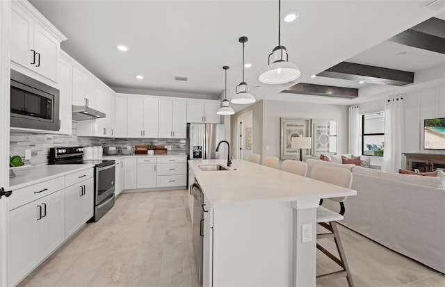 kitchen featuring appliances with stainless steel finishes, a sink, open floor plan, a breakfast bar, and under cabinet range hood