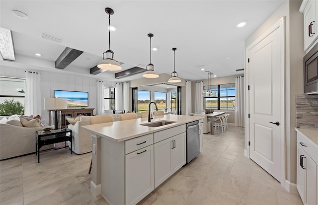 kitchen with white cabinets, a sink, dishwasher, light countertops, and open floor plan