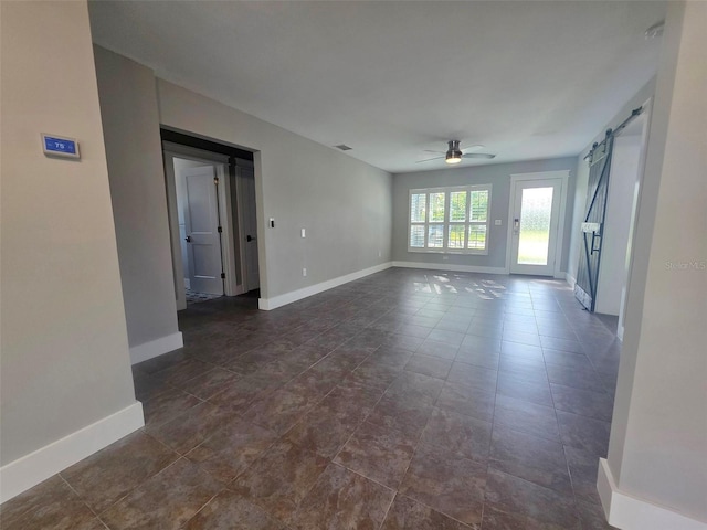 unfurnished room with baseboards, a barn door, a ceiling fan, and visible vents