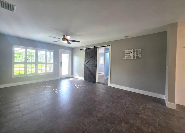 unfurnished room with baseboards, visible vents, a barn door, and a ceiling fan