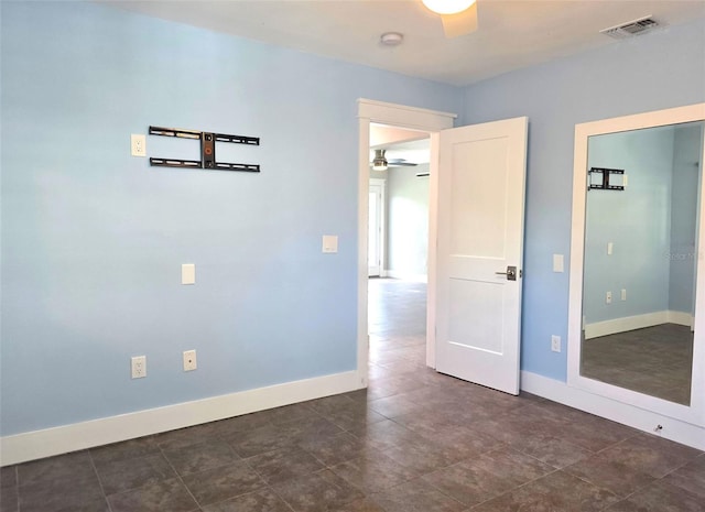 empty room featuring dark tile patterned flooring, ceiling fan, baseboards, and visible vents