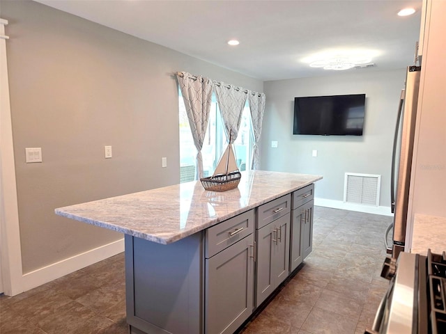 kitchen featuring gray cabinets, visible vents, recessed lighting, light stone countertops, and a kitchen island