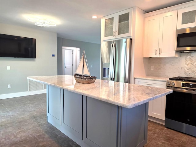 kitchen with a kitchen island, stainless steel appliances, white cabinets, and backsplash