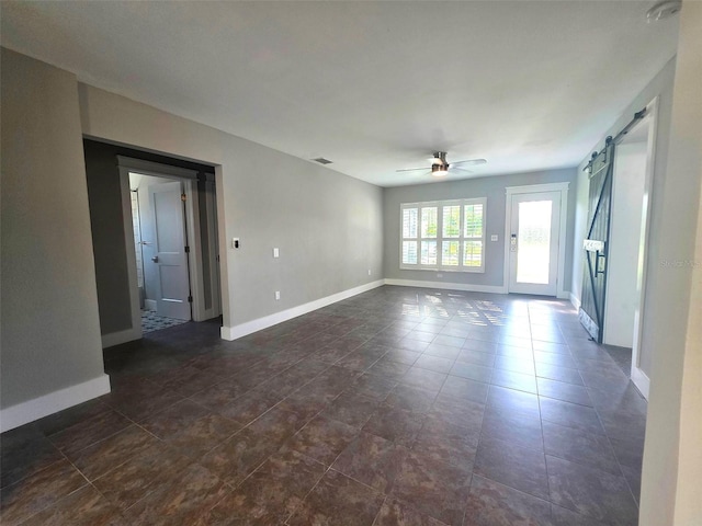 empty room with dark tile patterned flooring, visible vents, a barn door, baseboards, and ceiling fan