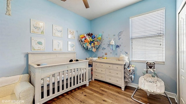 bedroom with a nursery area, baseboards, a ceiling fan, and light wood finished floors