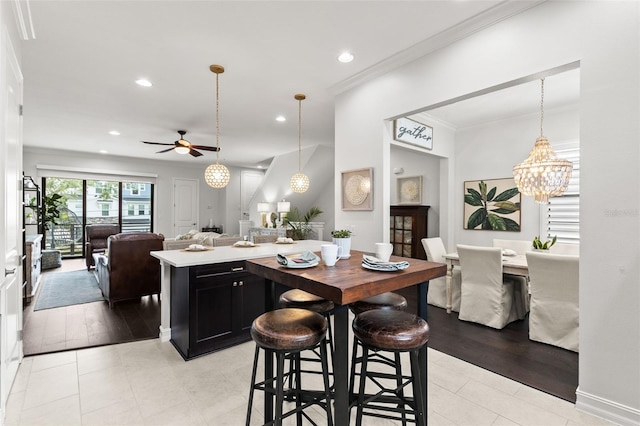 kitchen featuring dark cabinetry, light countertops, ceiling fan with notable chandelier, open floor plan, and ornamental molding