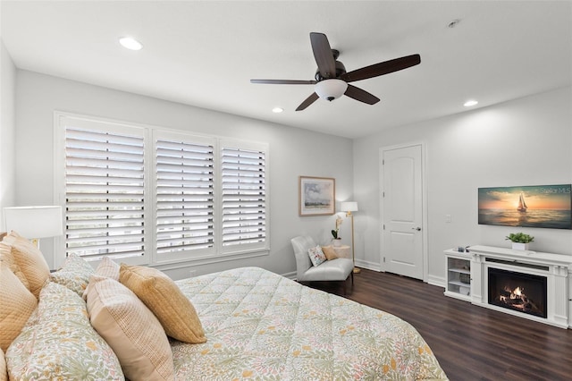 bedroom featuring a warm lit fireplace, ceiling fan, recessed lighting, baseboards, and wood finished floors