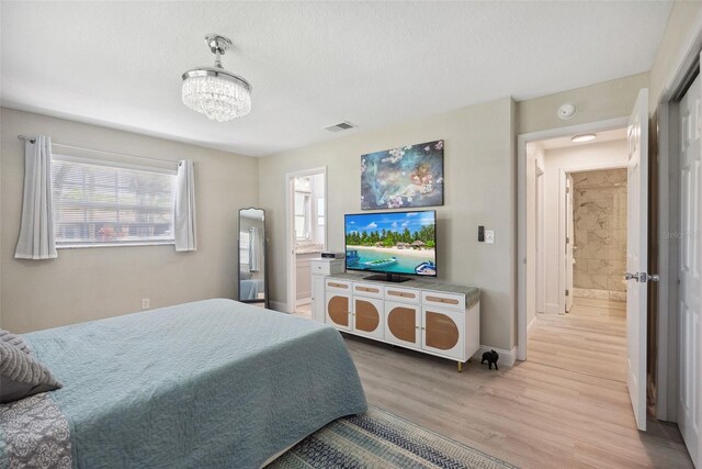 bedroom featuring visible vents, baseboards, an inviting chandelier, ensuite bathroom, and light wood-style flooring