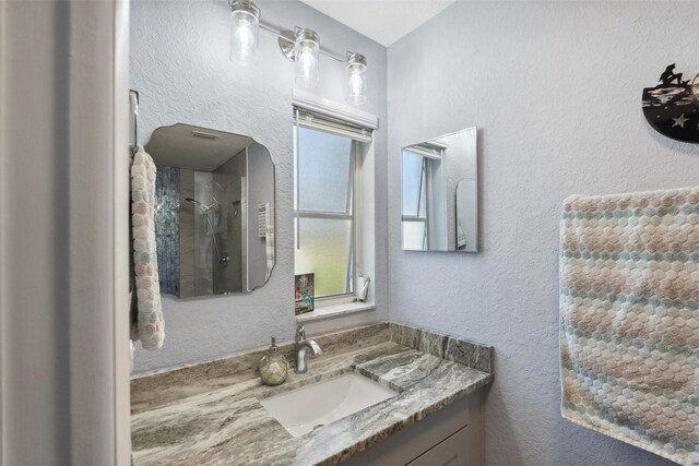 full bathroom featuring vanity, a textured wall, and walk in shower