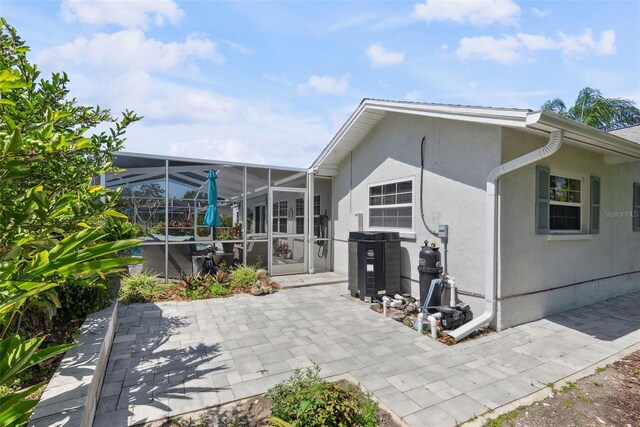 rear view of house with glass enclosure, a patio area, and stucco siding