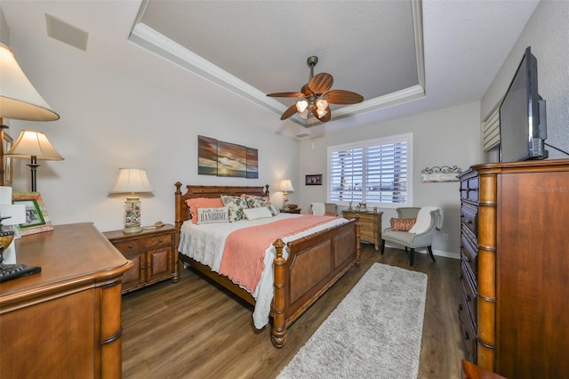 bedroom with a tray ceiling, visible vents, ceiling fan, and dark wood-type flooring