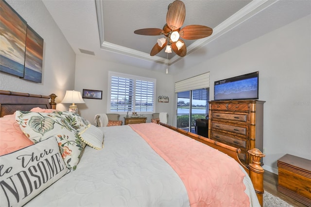 bedroom featuring a ceiling fan, visible vents, wood finished floors, a raised ceiling, and ornamental molding