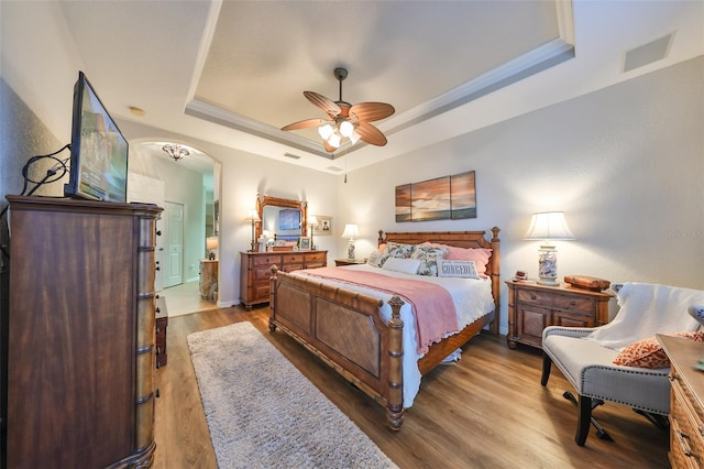bedroom with arched walkways, a tray ceiling, wood finished floors, and visible vents