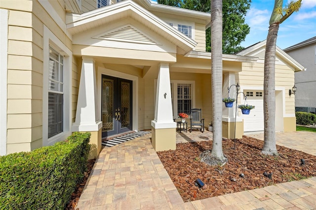 entrance to property featuring covered porch, driveway, french doors, and a garage