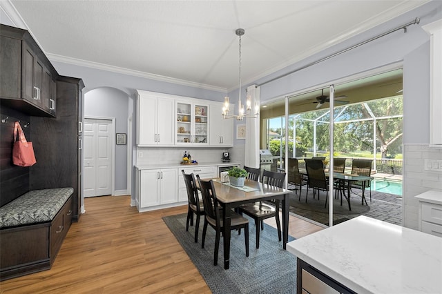 dining space featuring ornamental molding, light wood-style floors, ceiling fan, a sunroom, and arched walkways