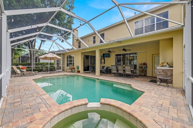 view of swimming pool featuring ceiling fan, a pool with connected hot tub, glass enclosure, a patio, and an outdoor kitchen