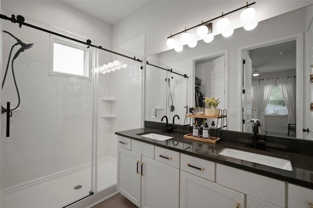 full bathroom with double vanity, a sink, a ceiling fan, and a stall shower