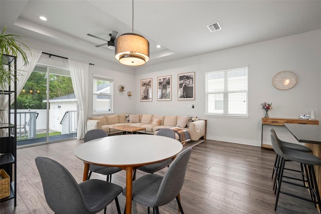 dining area featuring a ceiling fan, visible vents, wood finished floors, and a raised ceiling