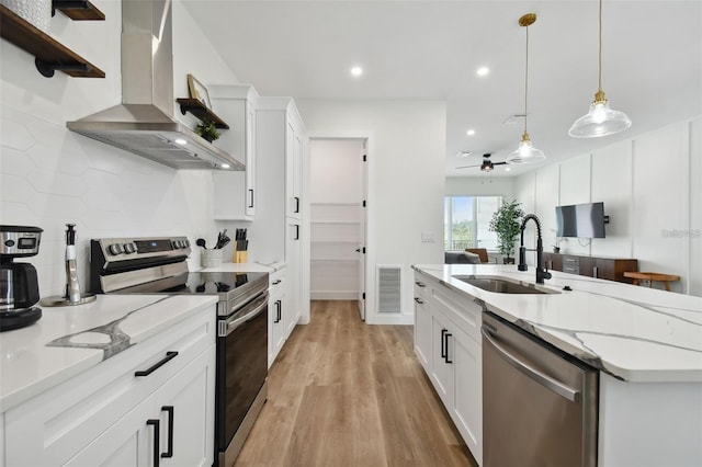 121 E Warren Ave Unit 1, Tampa, FL 33602 - kitchen featuring stainless steel appliances, wall chimney range hood, white cabinetry, decorative light fixtures, and light wood-type flooring
