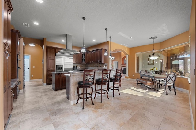 kitchen featuring decorative backsplash, visible vents, island range hood, arched walkways, and built in refrigerator