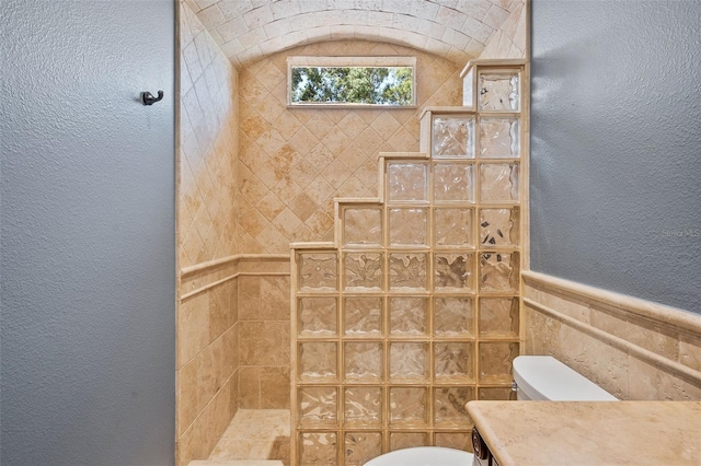 bathroom featuring a walk in shower, toilet, and a textured wall