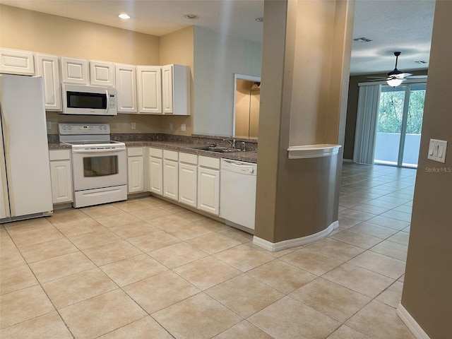 kitchen featuring light tile patterned flooring, dark countertops, white appliances, white cabinetry, and a sink