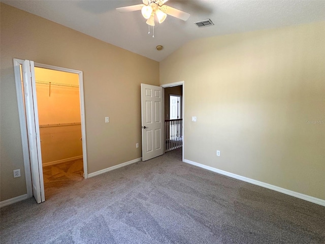 unfurnished bedroom with carpet flooring, a walk in closet, baseboards, lofted ceiling, and visible vents