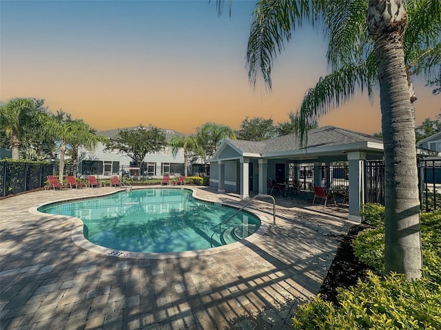 pool at dusk featuring a community pool, a patio, and fence