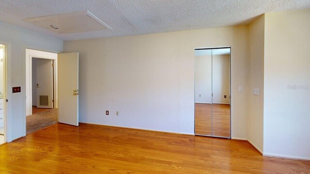 unfurnished room featuring baseboards, a textured ceiling, light wood-style flooring, and attic access