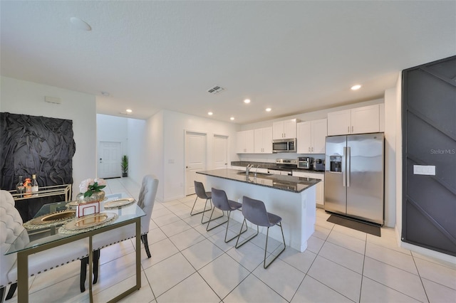 kitchen featuring a kitchen island with sink, white cabinets, a sink, light tile patterned floors, and stainless steel appliances