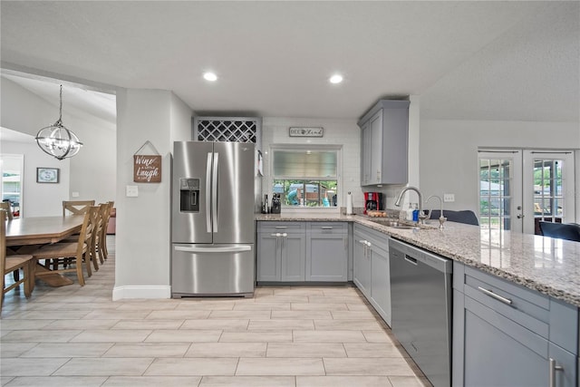 kitchen with a sink, a notable chandelier, gray cabinetry, appliances with stainless steel finishes, and light stone counters